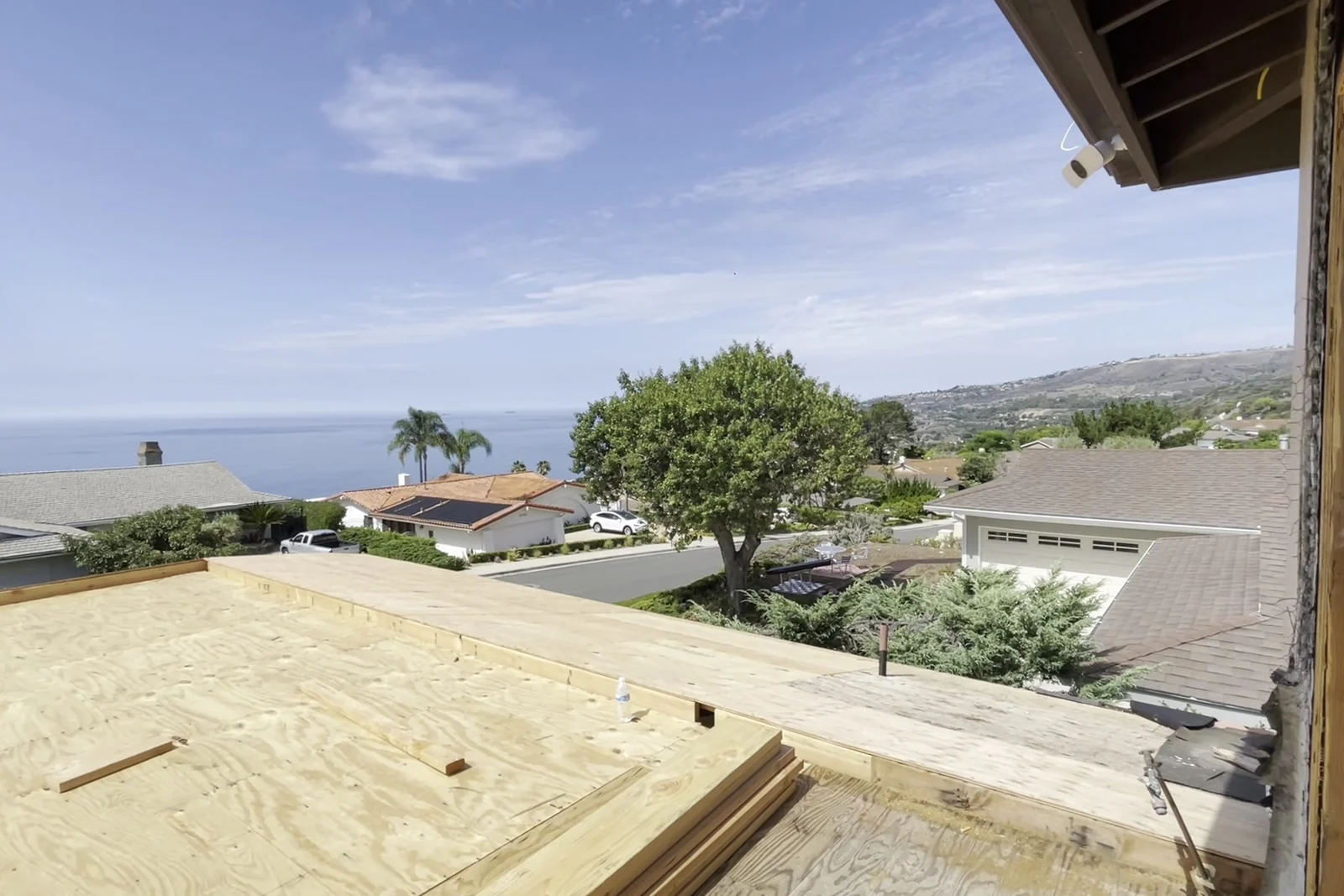The stripped roof deck and open framing looking out across neighbouring rooftops to the ocean horizon