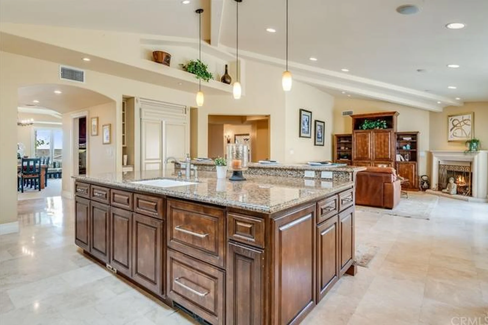 A closed kitchen with cherry-stained cabinetry and island, iron bar stools, a tumbled-tile backsplash, travertine floor and soffit downlights