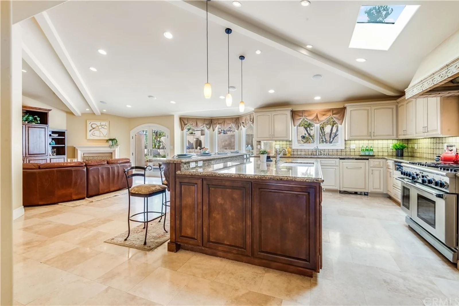 A cream raised-panel kitchen and family room under a vaulted ceiling with a skylight, valanced windows and tiled counters