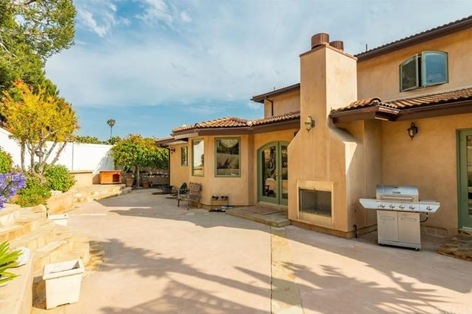 The original rear elevation with stucco arches, a heavy chimney mass, a built-in barbecue counter, terracotta paving and wrought-iron furniture